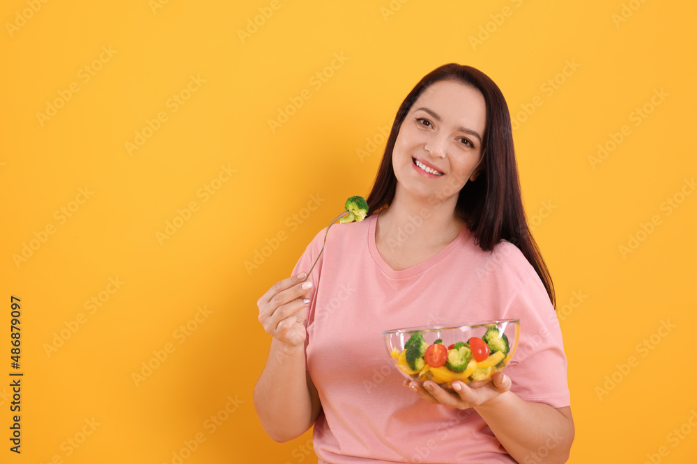 Beautiful overweight woman eating salad on yellow background, space for text. Healthy diet Beautiful overweight woman eating salad on yellow background, space for text. Healthy diet