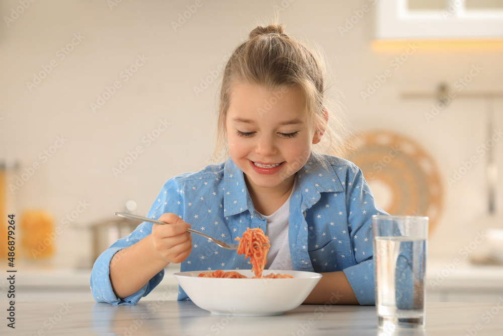 Cute little girl eating tasty pasta at table in kitchen Cute little girl eating tasty pasta at table in kitchen