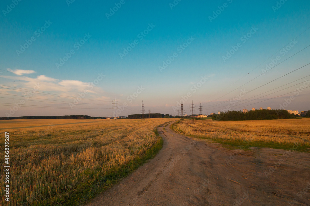 Harvested fields with cut straw and electivity power line columns in summer warm sunset evening light