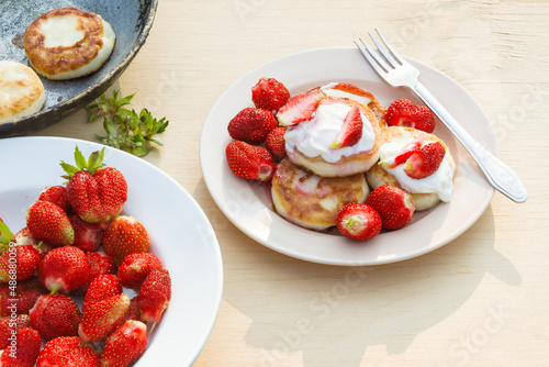 Cheesecakes with strawberries and sour cream. Breakfast in nature. Traditional Russian and Ukrainian dish.