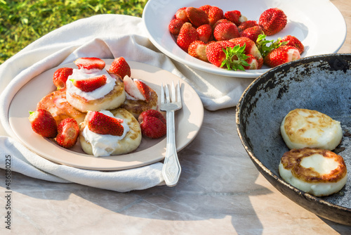 Cheesecakes with strawberries and sour cream. Breakfast in nature. Traditional Russian and Ukrainian dish.