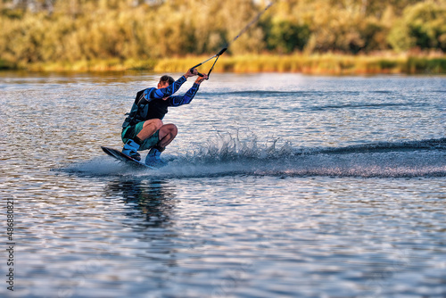 A man wakeboarding on a lake on summer day in a life jacket. Soft focus. Action blur.
