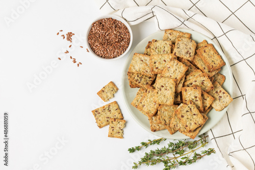 Square diet cookies with thyme, flax seeds and spices  in a light plate on white background. Crunchy herbal crackers top view with copy space