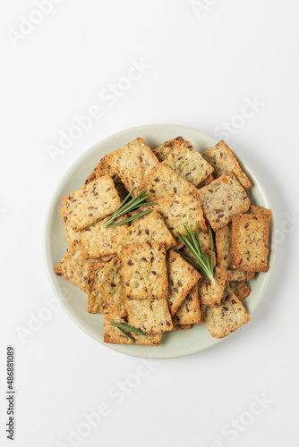 Square diet cookies with rosemary, flax seeds and spices  in a light plate on white background. Crunchy herbal crackers top view