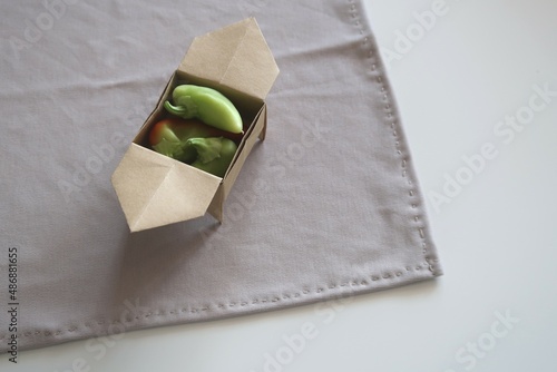 Craft brown sanbo origami box on grey fabric tissue on the white table. Japanese traditional Origami paper box with legs Sanbo. Still life box origami with small tiny red and green bell pepper inside photo