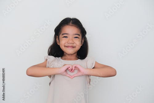 Asian kid smiling with her hand making heart shape on chest photo