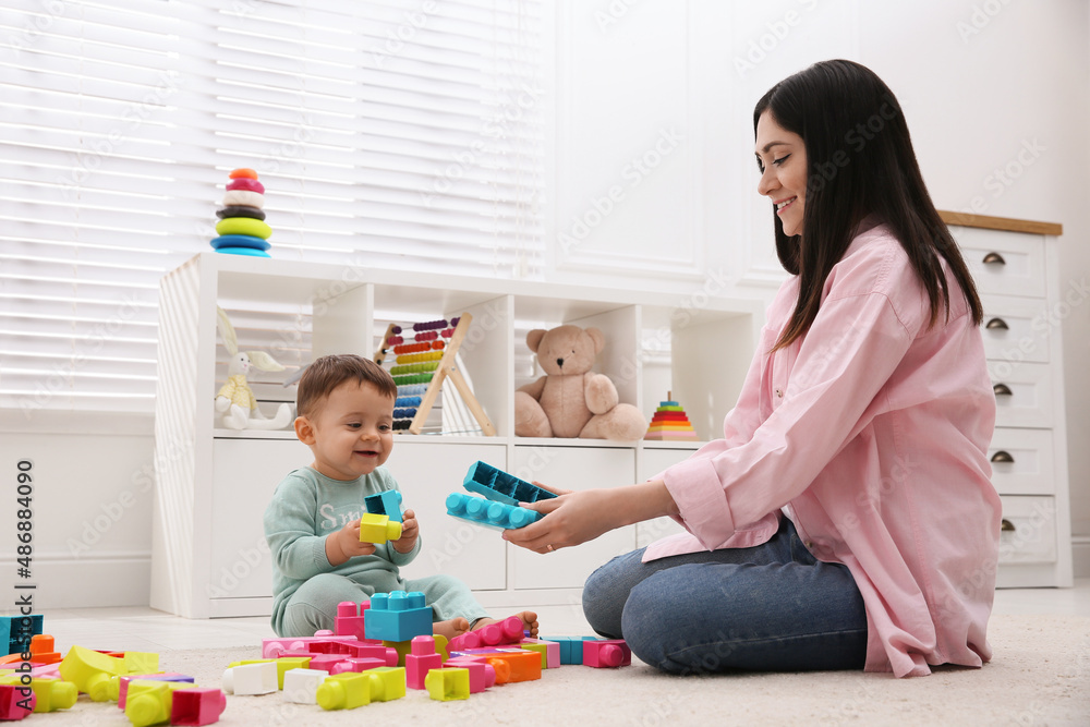Naklejka premium Cute baby boy playing with mother and building blocks on floor at home