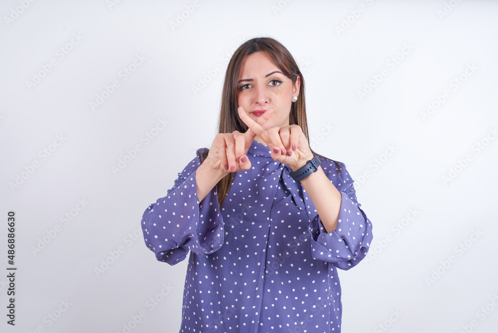Young arab woman wearing polka-dot clothes over white backgtound has rejection angry expression crossing fingers doing negative sign. Young arab woman wearing polka-dot clothes over white backgtound has rejection angry expression crossing fingers doing negative sign.