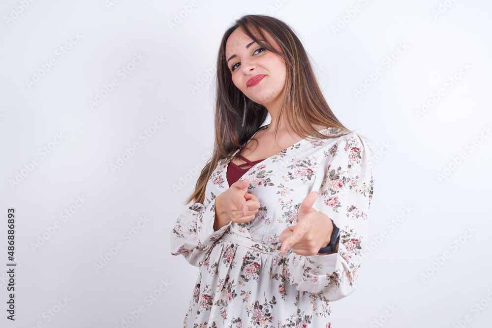 Hey you, bang. Joyful and charismatic good-looking Young arab woman wearing floral shirt over white backgtound winking and pointing with finger pistols at camera happily and cheeky. Hey you, bang. Joyful and charismatic good-looking Young arab woman wearing floral shirt over white backgtound winking and pointing with finger pistols at camera happily and cheeky.
