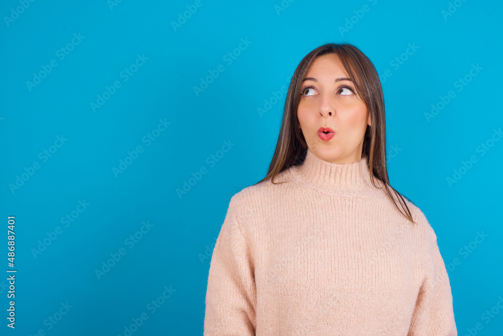 Shocked Young arab woman wearing knitted sweater over blue backgtound look empty space with open mouth screaming: Oh My God! I can't believe this. Shocked Young arab woman wearing knitted sweater over blue backgtound look empty space with open mouth screaming: Oh My God! I can't believe this.