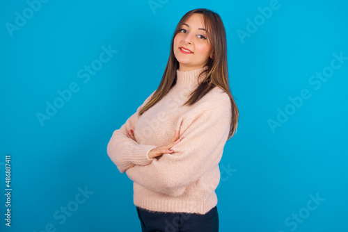 Portrait of Young arab woman wearing knitted sweater over blue backgtound standing with folded arms and smiling