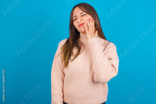 Fotografía Young arab woman wearing knitted sweater over blue backgtound  with toothache