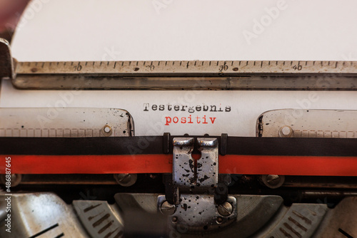 The German word test result positive written with an old mechanical typewriter with red and black ribbon in black and red color on a white sheet of paper