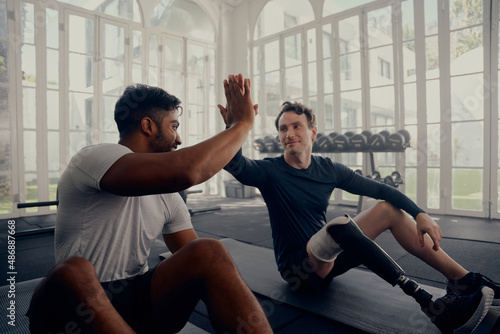 Two friends training in the gym - one with a prosthesis . Two men high fiving in the gym after a good training session photo
