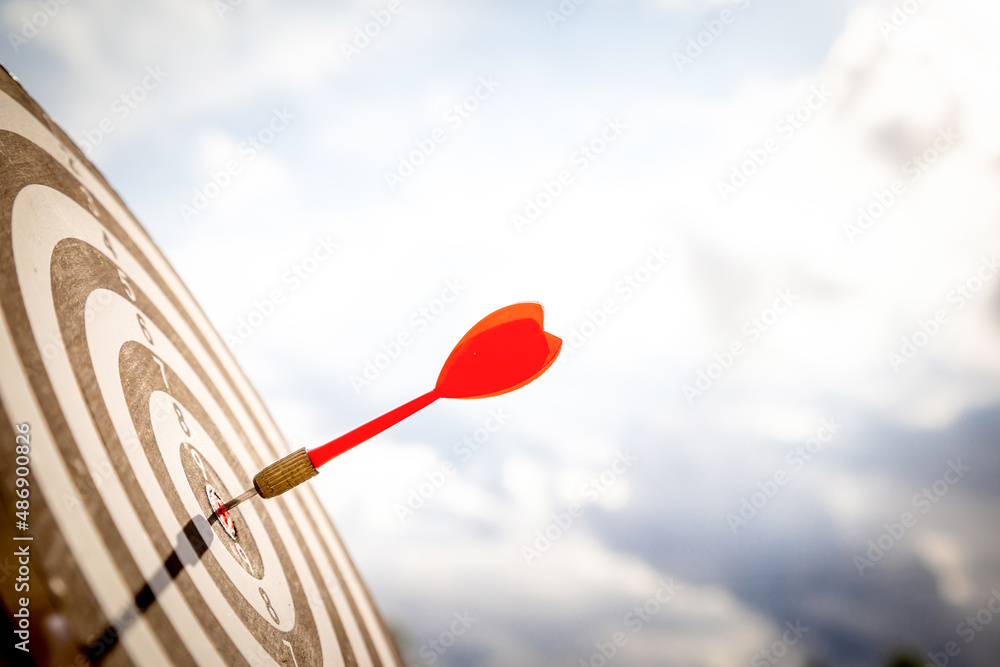 Close up shot red darts arrows in the target of dartboard center on dark blue sky background. Business target or goal success and winner concept. Close up shot red darts arrows in the target of dartboard center on dark blue sky background. Business target or goal success and winner concept.