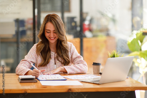 Portrait of Asian businesswoman with laptop writes on a document at the coffee shop, Asian woman  doing planning analyzing the financial report, business plan investment, finance analysis concept © David