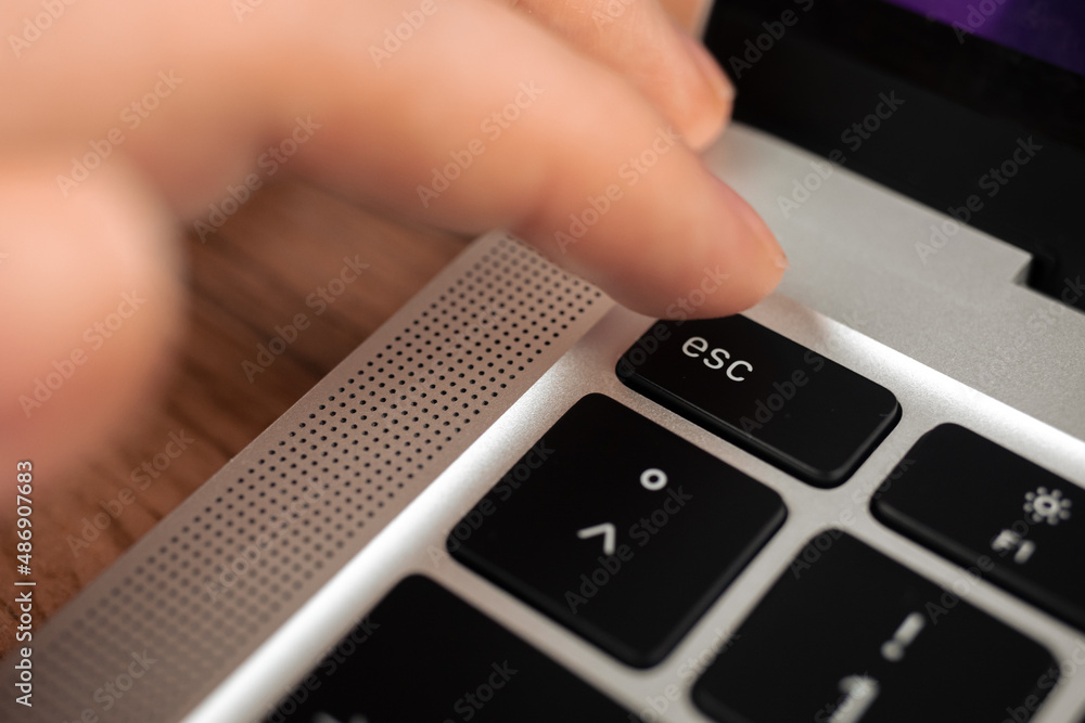 Hand pressing escape key on modern laptop keyboard. Esc sign and symbol