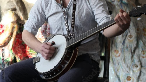 Male musician playing banjo sitting chair indoor.