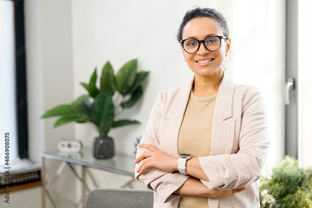 Cheerful woman entrepreneur stands with arms crossed in the contemporary office, multiracial freelancer woman in smart casual wear looks at the camera with arms crossed, small business owner Cheerful woman entrepreneur stands with arms crossed in the contemporary office, multiracial freelancer woman in smart casual wear looks at the camera with arms crossed, small business owner