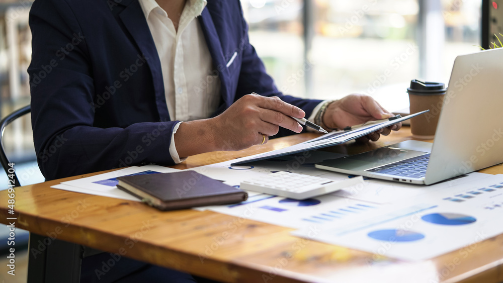 Male businessman analyzes income charts and business graphs and strategy ideas, hand holding pen pointing financial paper charts.. Male businessman analyzes income charts and business graphs and strategy ideas, hand holding pen pointing financial paper charts..