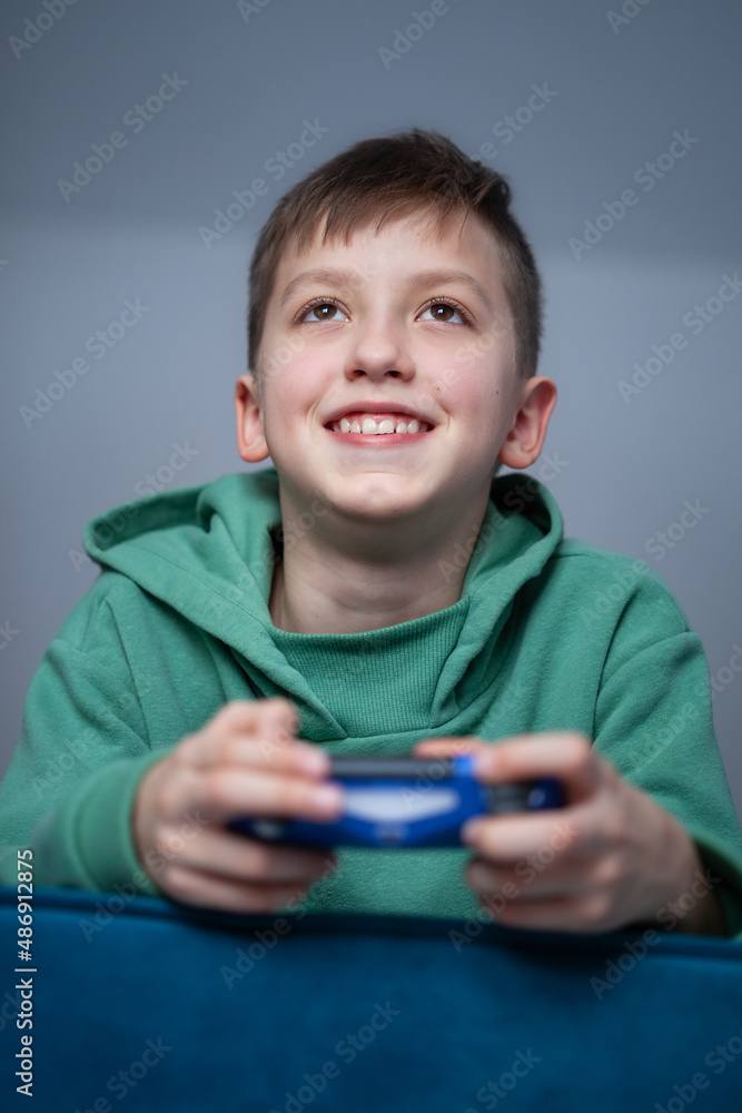 Boy on the couch plays video games using a controller. The child smiles, holding a joystick in his hands Boy on the couch plays video games using a controller. The child smiles, holding a joystick in his hands