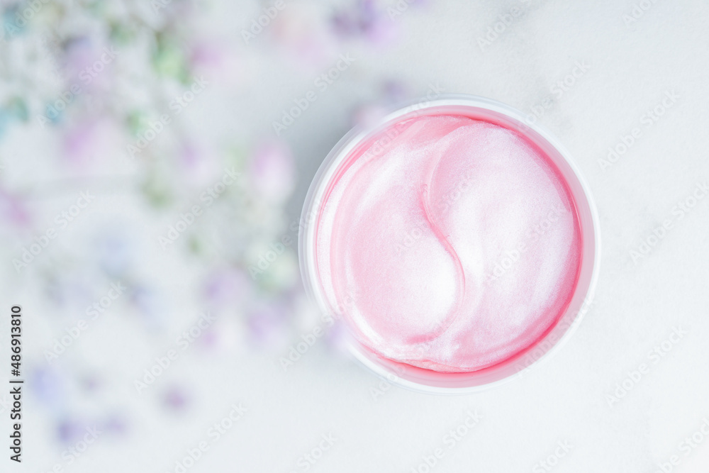 Pink patches on a marblel background next to pastel flowers. Natural flower extract cosmetics, beauty and fashion. Patches for moisturizing in a jar, flat lay, top view. Pink patches on a marblel background next to pastel flowers. Natural flower extract cosmetics, beauty and fashion. Patches for moisturizing in a jar, flat lay, top view.