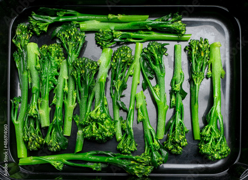 Fresh long-stem broccoli, broccolini steam-blanched, deep frozen and thawing in black dish. Top down view. photo