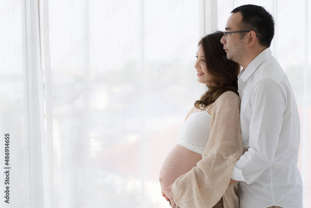 Asian Pregnant Couple Standing by Window and Looking Out Asian Pregnant Couple Standing by Window and Looking Out