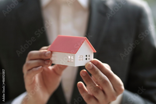 Close up of businessman holding model house. Architecture, building, construction, real estate and property concept 