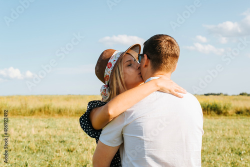 Pretty young woman in astraw hat hugs and kisses man outdoors on sunny day. Caucasian heterosexual love couple flirting in nature, romantic relationship photo
