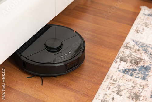 Robot vacuum cleaner cleaning a wooden parquet in living room.