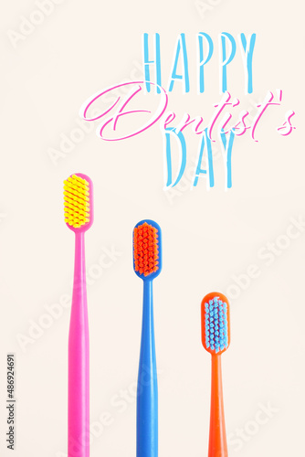 greeting card three multi-colored toothbrushes on a beige background and the inscription happy dentists day. copy space..