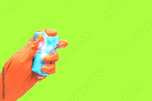 a hand in an orange rubber glove and a blue sponge with foam on a green background..