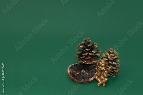 Weihnachtsdekoration. Kleine goldene Engelsfigur mit goldener Dekoration aus Tannenzapfen auf einem grünen Hintergrund