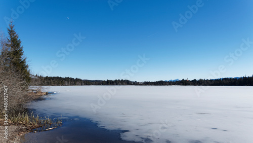 Kirchsee zugefrorener See im tiefen Winter, mystischer Moorsee mit Blick auf Kloster Reutberg und Benediktenwand in den Bayerischen Voralpen
