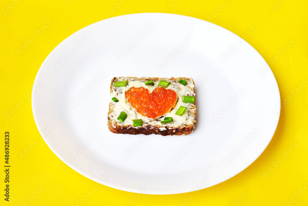 bread with butter, green onion and fish caviar on a white plate and yellow background bread with butter, green onion and fish caviar on a white plate and yellow background