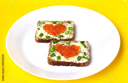 bread with butter and caviar from fish on a white plate and yellow background
