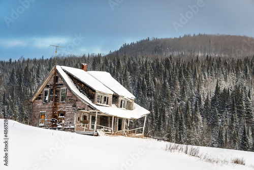 Old Farmhouse with fresh snow covering evergreen trees on a nearby hillside.  © John