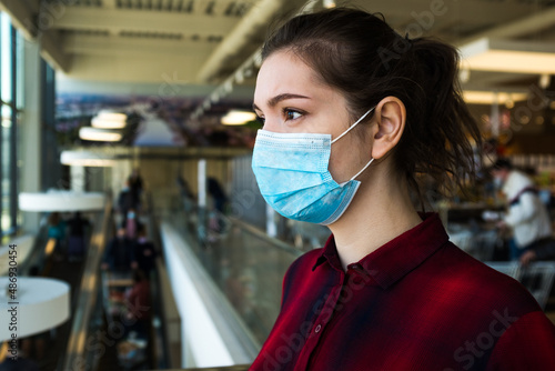 Beautiful pretty worried caucasian young woman wearing protective surgical face mask, standing in a shopping mall or supermarket, stressed and anxious about the future, Coronavirus COVID-19 lifestyle