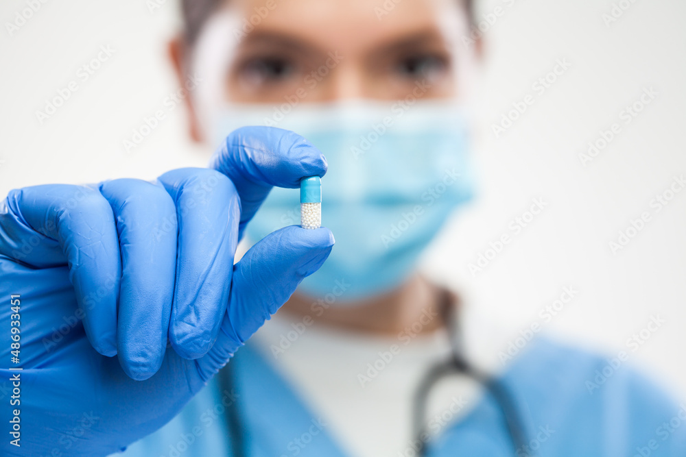 Female UK NHS GP ICU general practitioner doctor wearing protective face mask holding antibiotic pill Female UK NHS GP ICU general practitioner doctor wearing protective face mask holding antibiotic pill