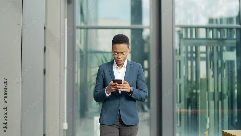 business black woman walking on city street downtown look and use mobile phone. African American female employee entrepreneur read screen smartphone on urban background. confident office worker business black woman walking on city street downtown look and use mobile phone. African American female employee entrepreneur read screen smartphone on urban background. confident office worker