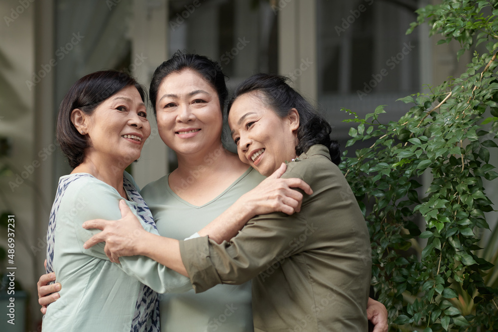 Portrait of smiling senior women hugging and looking at camera, old friends reunion concept