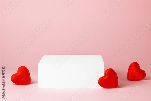 White square podium with red hearts on a pink background. Advertising and product presentation. Valentine's Day and 14 February. Mockup for cosmetics.