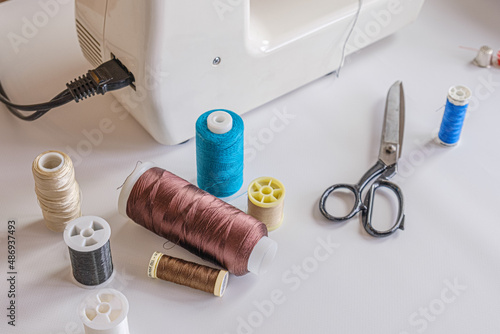 Spools of multi-colored thread and scissors on the table next to the electric sewing machine