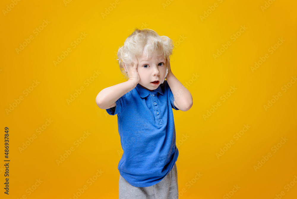 A little caucasian boy is talking on the phone, he grabbed his head with his second hand from the news he heard, he is surprised and dumbfounded. Yellow background. A little caucasian boy is talking on the phone, he grabbed his head with his second hand from the news he heard, he is surprised and dumbfounded. Yellow background.