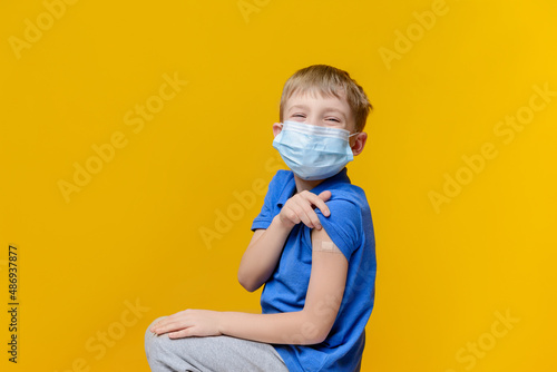 A kid in a mask shows his hand with a band-aid after receiving a dose of the vaccine. The child is vaccinated. He is happy that he is protected from the terrible virus.