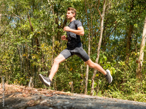 Side view, handsome Caucasian athlete runner running on trail uphill mountain in natural park.