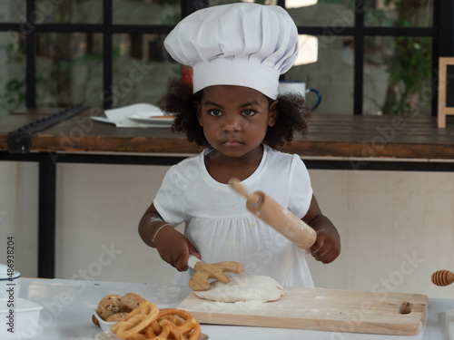 Cute little African girl wearing chef hat playing with baking dough.