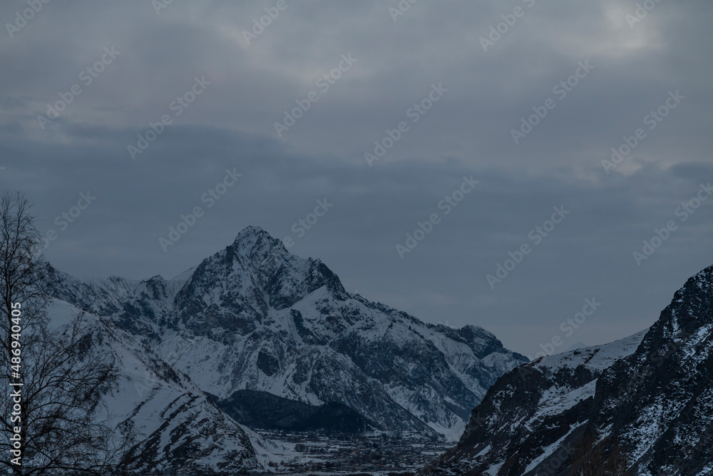 Beautiful winter mountain landscape at the sunrise with dramatics clouds. High snow covered mountains in the fog. 