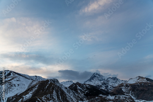 Panoramic view of the high snow covered mountain Kazbek at the sunrise. Winter mountains landscape. Georgia, Kazbegi.